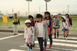 画像：見守り隊ひまわりの方に見守られて横断歩道を渡る児童ら